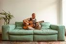 Lucas Santtana, assis sur un canapé, jouant de la guitare