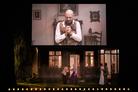 Un comédien dans une maison surplombée d'un écran géant diffusant l'image d'un homme